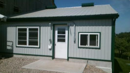 The outside of a milk house. The door is closed and a outer flap covers the hose port.